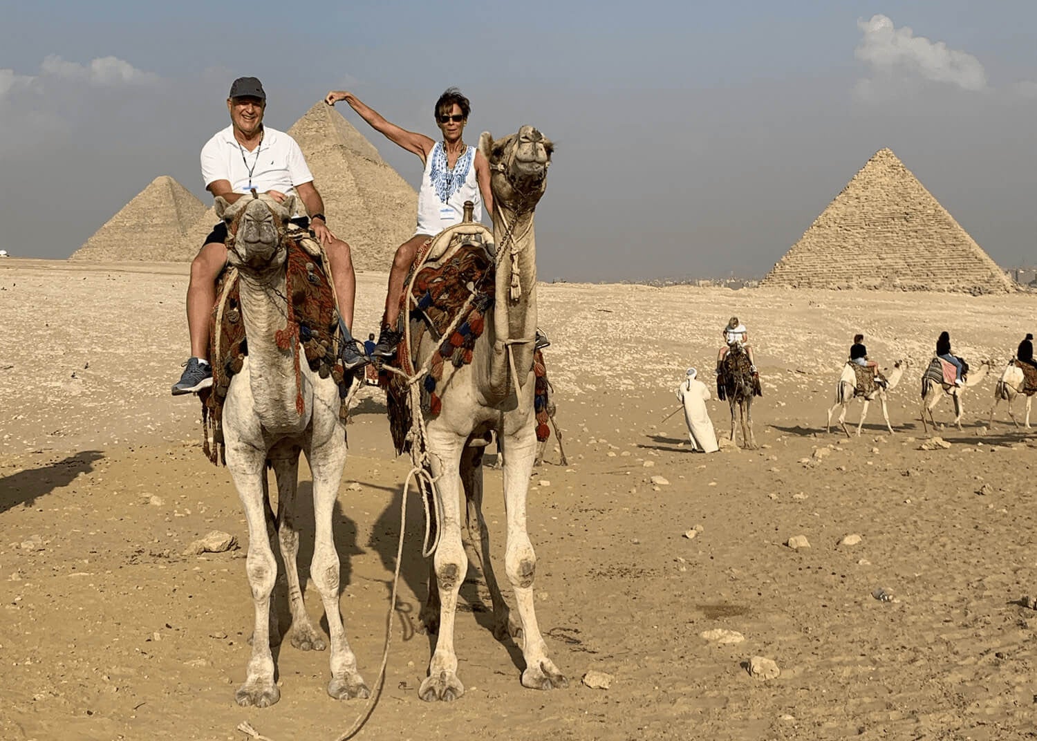 Guests riding camels in front of Great Pyramid and Giza Plateau